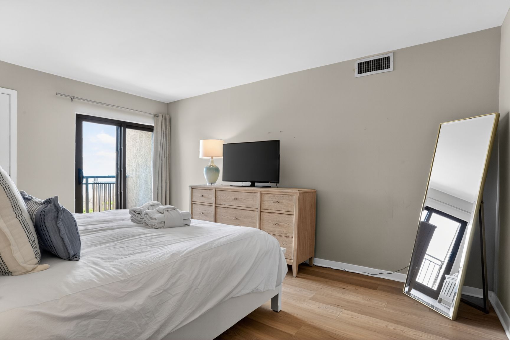 A hotel room with a bed, a TV on a wooden dresser, a mirror, and a balcony view.