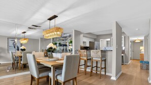 Un comedor moderno con una mesa y sillas de madera, una araña y una cocina al fondo.