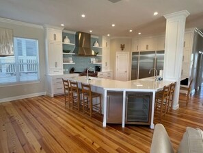 A spacious kitchen with white cabinetry, a central island with bar stools, and a stainless steel range hood.