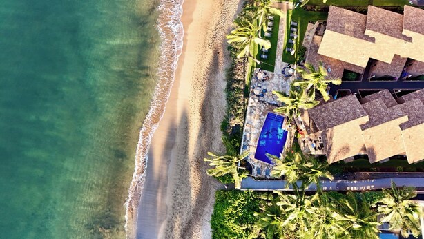Vista aérea de um resort com praia, piscina e palmeiras.