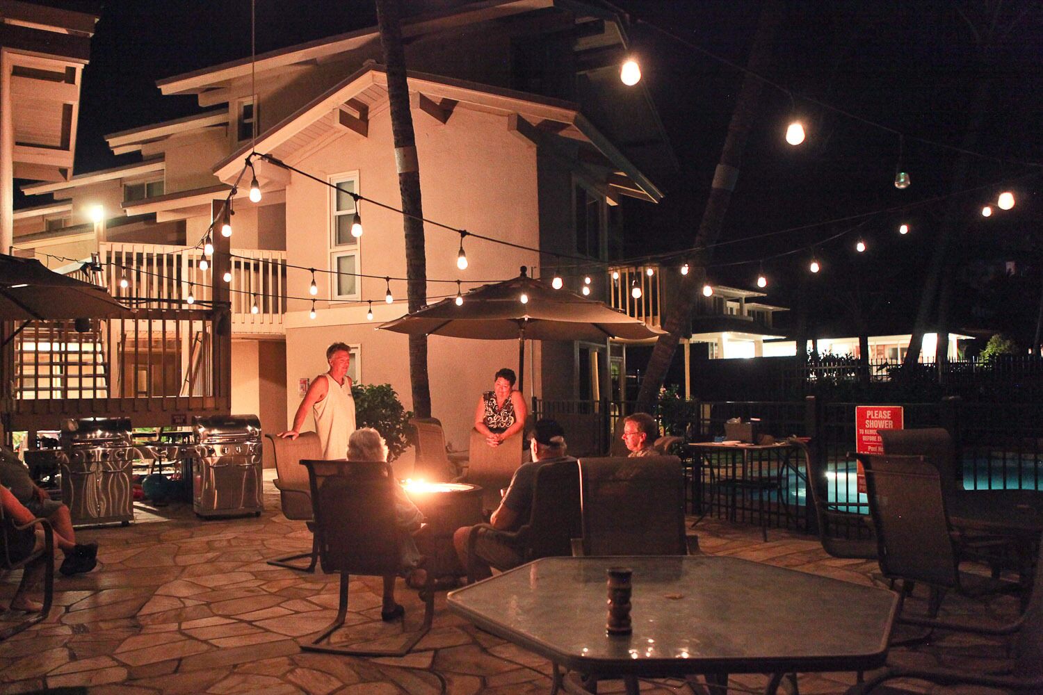 Eine Außenpatio-Terrasse mit Tischen, Stühlen, Lichterketten und einem Pool im Hintergrund.