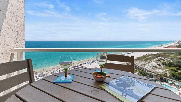 Un balcón con vista a la playa y al océano, dos copas de vino, un cuenco y una revista.