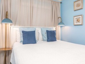 A neatly made bed with two pillows, a bedside lamp, and a curtain.