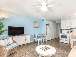 A compact living space with a kitchenette, a dining area, a seating area with a sofa, and a television.