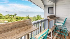 Ein Balkon mit hölzernen Bänken und Stühlen, der auf ein Gewässer blickt.