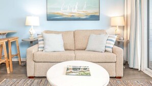 Ein Wohnzimmer mit einem beigefarbenen Sofa, zwei Nachttischen mit Lampen, einem runden Couchtisch mit einer Zeitschrift und einem Segelboot-Gemälde an der Wand.