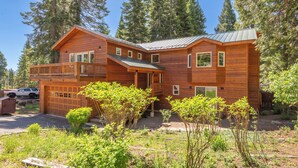A two-story wooden cabin with a balcony, a garage, and a garden area. - Luxury Family Home, Hot Tub, Garage, Family Room, Near Tahoe City in Carnelian Bay (Carnelian Bay)