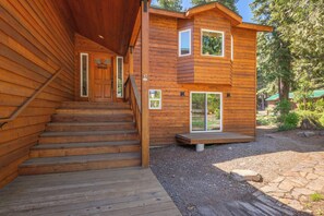 A wooden cabin with a staircase leading to a front door, a deck, and a stone pathway. - Luxury Family Home, Hot Tub, Garage, Family Room, Near Tahoe City in Carnelian Bay (Carnelian Bay)