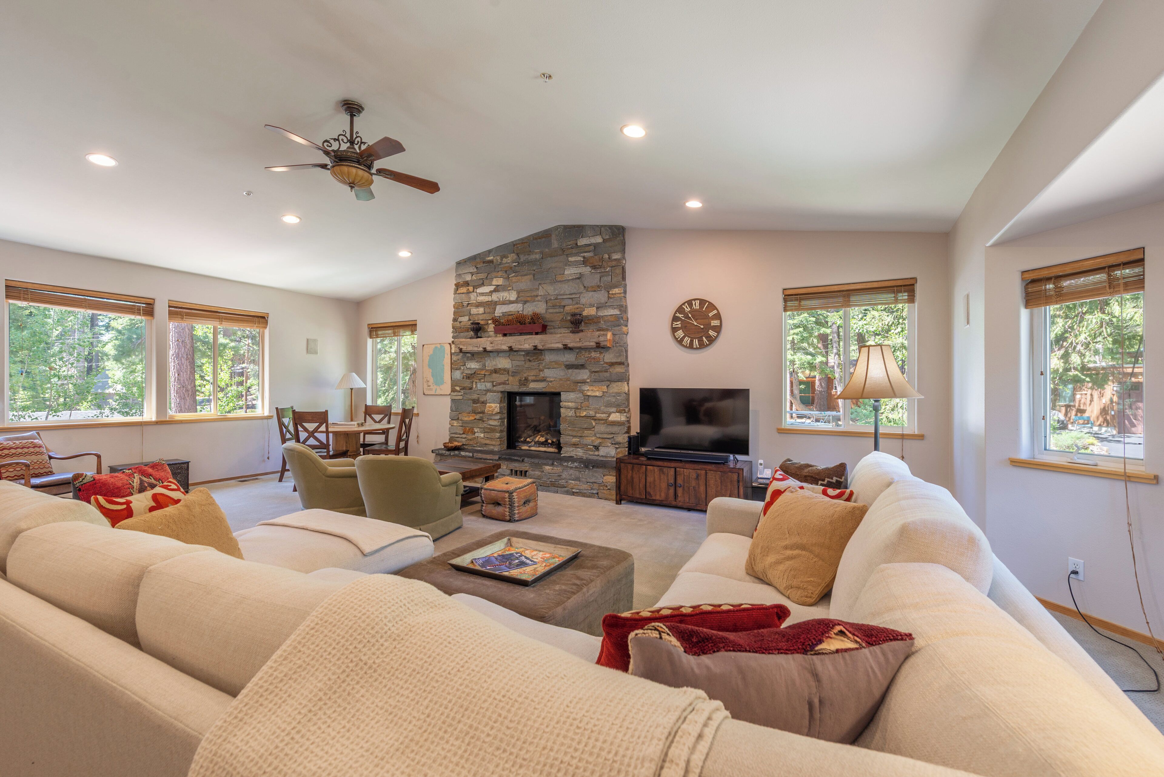 A spacious living room with a stone fireplace, comfortable seating, and large windows.