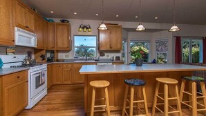 A kitchen with wooden cabinets, a white stove, a large island with stools, and pendant lighting. - Garden Pond Retreat~Hot tub & Fire Pit! (Mckinleyville)