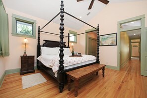 A four-poster bed with a wooden bench, a nightstand, and a lamp.