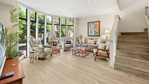 A spacious living room with large windows, a staircase, and a cozy seating area. - The Residences at Napili Bay 8  Townhome In Lush Tropical Setting (Lahaina)
