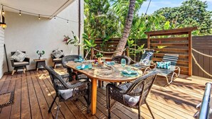 An outdoor patio with a wooden table set for dining, wicker chairs, and a wooden fence with a rope barrier. - The Residences at Napili Bay 8  Townhome In Lush Tropical Setting (Lahaina)