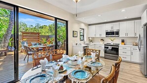 A modern kitchen with white cabinets, stainless steel appliances, and a dining area with a glass table set for six. - The Residences at Napili Bay 8  Townhome In Lush Tropical Setting (Lahaina)