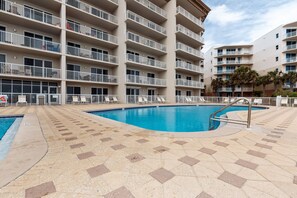 A swimming pool with a tiled deck, surrounded by a multi-story building with balconies.