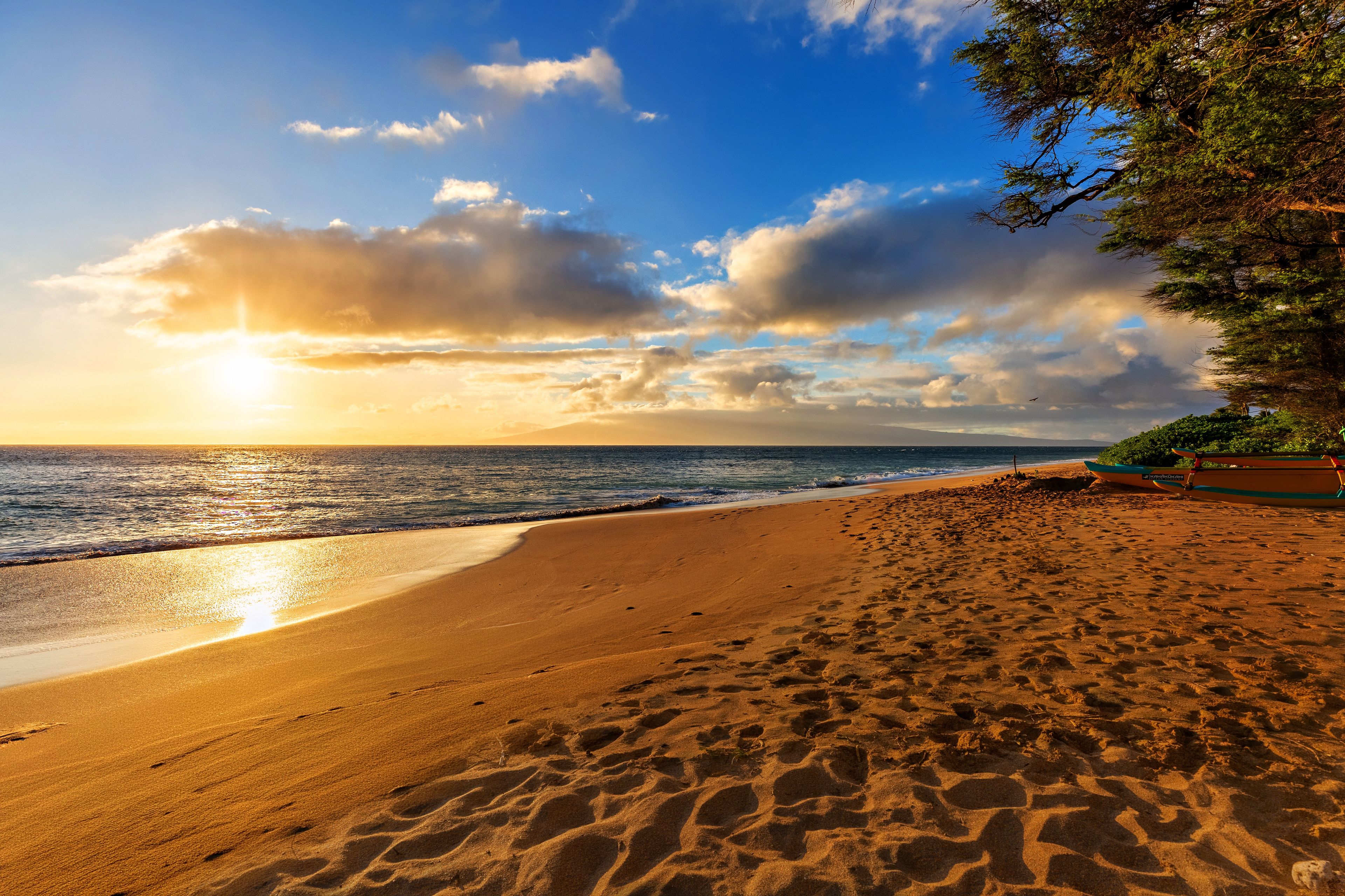 A beach with footprints leading to the water, a boat, and a clear sky.