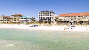 Un hotel frente a la playa con varios pisos, una playa de arena y agua cristalina.