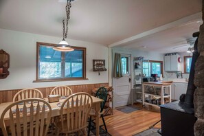 A dining area with a wooden table and chairs, a hanging light fixture, and a window with blinds.