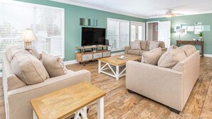 A living room with two sofas, a coffee table, a TV, and a ceiling fan. - Dune Villa | Mid Island, 3 Living and Kitchen Spaces in One Villa (Tybee Island)