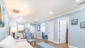 A spacious living room with a sofa, ottoman, and a dining area with chairs and a table. - Dune Villa | Mid Island, 3 Living and Kitchen Spaces in One Villa (Tybee Island)