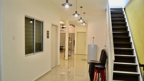 Un couloir avec un escalier sur la droite, un coin repas avec des chaises et une table, et des suspensions lumineuses qui pendent du plafond.