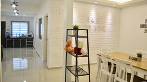 Une cuisine moderne avec un mur en briques blanches, un coin repas avec une table en bois et des chaises blanches, et une étagère en métal noir sur laquelle sont posés un ours en peluche et une plante.