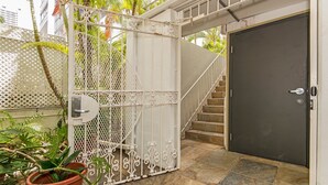 Una entrada cerrada con un portón metálico, una puerta oscura y una escalera que sube a un nivel superior.