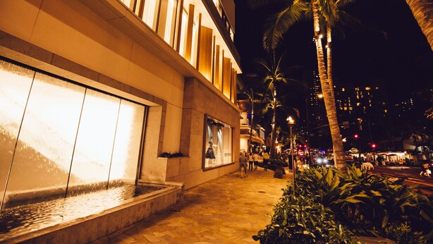 Vista nocturna de un hotel con fuente, palmeras y un camino pavimentado.