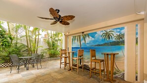 Un patio al aire libre con ventilador de techo, una mesa y sillas, y un mural de una playa.