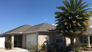 A single-story house with a garage, a driveway, and a well-maintained front yard with a palm tree and flowering plants.