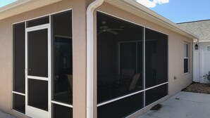 A covered patio with sliding glass doors, a ceiling fan, and a white fence in the background.