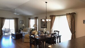 A spacious living room with a dining area, featuring a chandelier, a sofa set, and a large window with curtains.