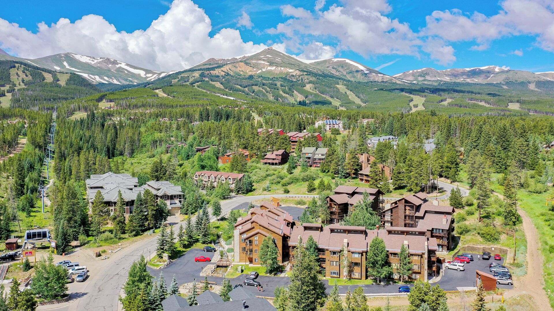 A mountain lodge with multiple buildings, a parking area, and a ski lift.