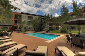 A pool area with lounge chairs and umbrellas, surrounded by buildings and trees. - Cozy Condo in River Run Village, King Bed, Walk to Gondola, Shops and Dining (Keystone)