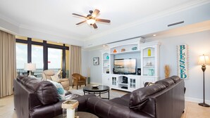 A living room with leather sofas, a TV, and a ceiling fan. - The Oasis At Orange Beach 1911 by Liquid Life (Orange Beach)