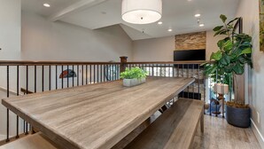 A spacious room with a long wooden table, a hanging light fixture, a staircase, and a large potted plant. - Central Location, Perfect for Large Groups & Recreation! Park City Woodside Ski Estate (Ski-in/out) (Park City)