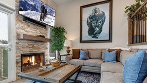 A living room with a fireplace, a sofa, a coffee table, and a television mounted on the wall. - Central Location, Perfect for Large Groups & Recreation! Park City Woodside Ski Estate (Ski-in/out) (Park City)