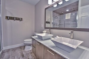 A modern bathroom with a large mirror, two vessel sinks, a toilet, and a wooden vanity.