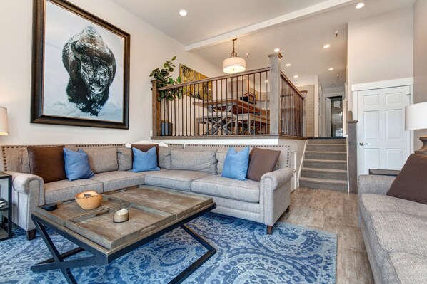 A living room with a sectional sofa, a coffee table, and a large painting of a bison.