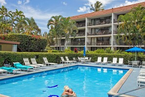 A hotel pool area with lounge chairs and a building with balconies.