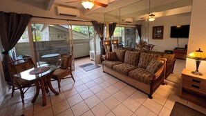 A living room with a sofa, a dining table with chairs, a ceiling fan, and a TV on the wall.