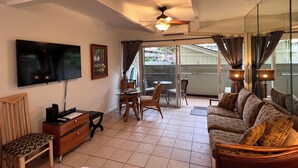 A living room with a TV, wooden furniture, a ceiling fan, and a view through a glass door.