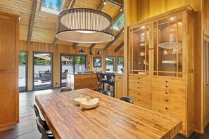 A spacious kitchen with a large wooden table, modern pendant lights, and a view to the outdoors. - 2 Pioneer - Designer Touches, Quiet South End, Gorgeous Kitchen, Hot Tub (Sunriver)