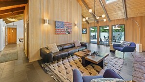 Ein modernes Wohnzimmer mit einer Ledersofa, einem Couchtisch und einem Schachspiel. Ein großes Fenster bietet einen Blick ins Freie.