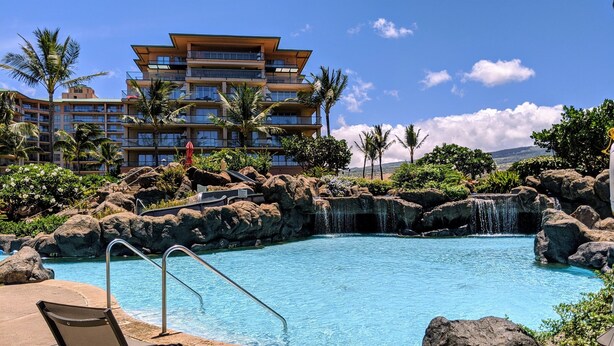A hotel with a pool surrounded by rocks and palm trees, with a waterfall feature.