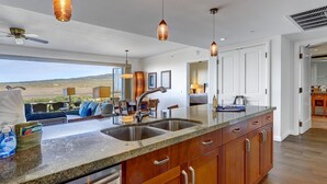 A modern kitchen with a large island, stainless steel sink, and pendant lighting.