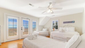 Un dormitorio con dos camas, ventilador de techo y vistas al exterior a través de amplios ventanales.