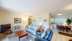 A living room with a sofa, a coffee table, a TV, and a dining area with a table and chairs.