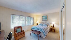 A bedroom with a bed, two bedside tables, a chair, and a window with blinds.