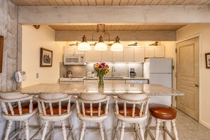 A kitchen with a central island, bar stools, a microwave, a coffee maker, and a telephone.